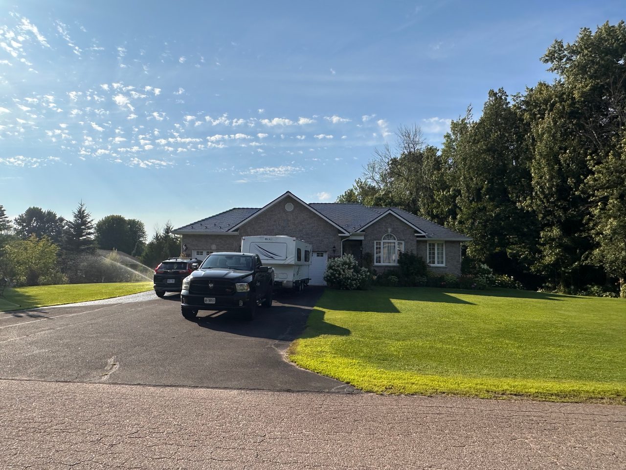 Ranch-style brick home with Interlock deep charcoal cedar shingle metal roof, multi-hip profile, viewed from front elevation on a sunny summer day.