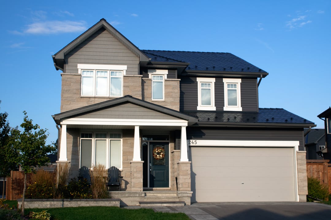 Two-storey Craftsman home in Carleton Place, ON with black Interlock aluminum slate metal roofing, stone and grey siding exterior.
