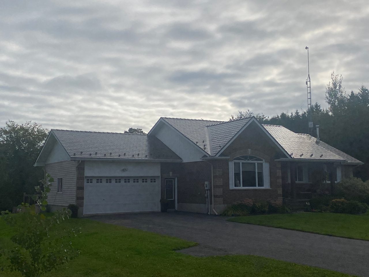 Ranch-style brick home in Winchester ON featuring Interlock Tudor Brown aluminum slate metal roofing with multi-gable complex roof profile under overcast skies.