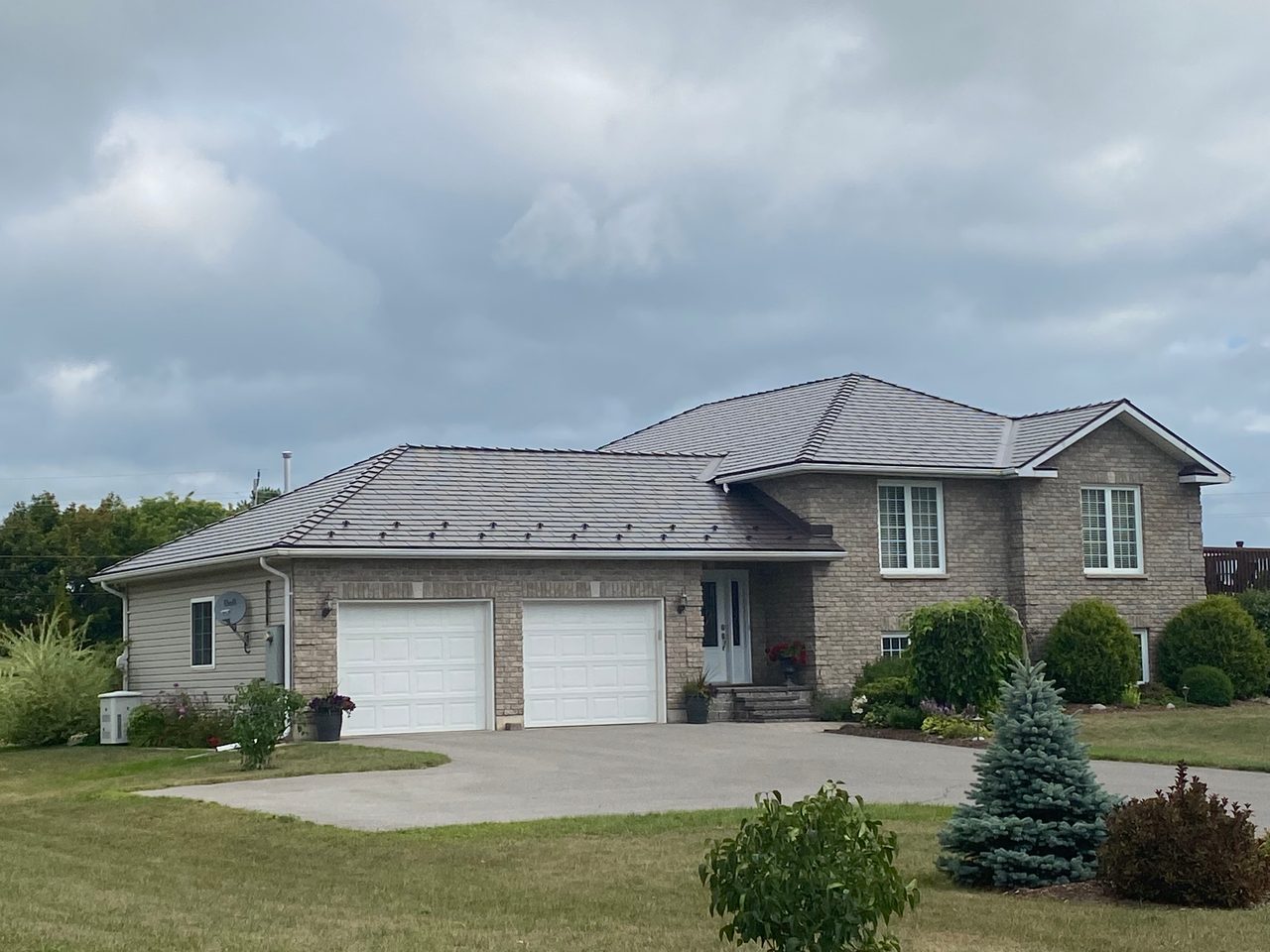 Front-left view of a rural Ontario home with Interlock Tudor Brown cedar shingle aluminum metal roofing on a multi-hip complex roofline over brick exterior.