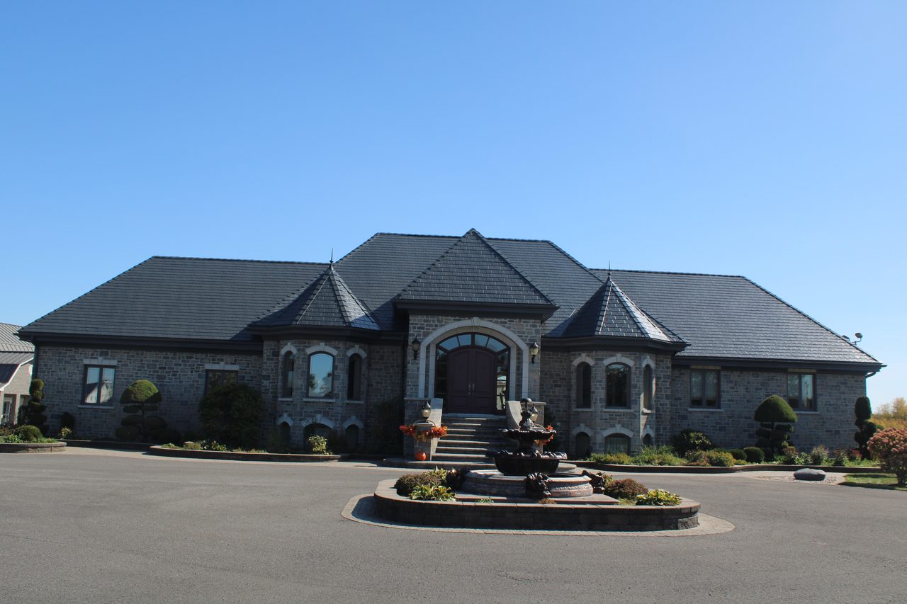 Grand single-storey stone estate in Alexandria ON featuring Interlock deep charcoal aluminum slate roofing with turreted hip roof and circular fountain driveway.
