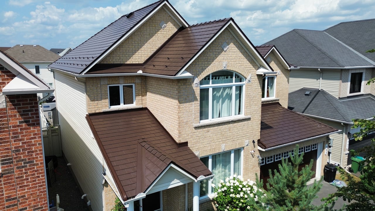 Aerial front view of a 2-storey suburban home with Interlock Colonial Brown aluminum slate metal roofing, complex multi-gable roof, and light brick exterior.