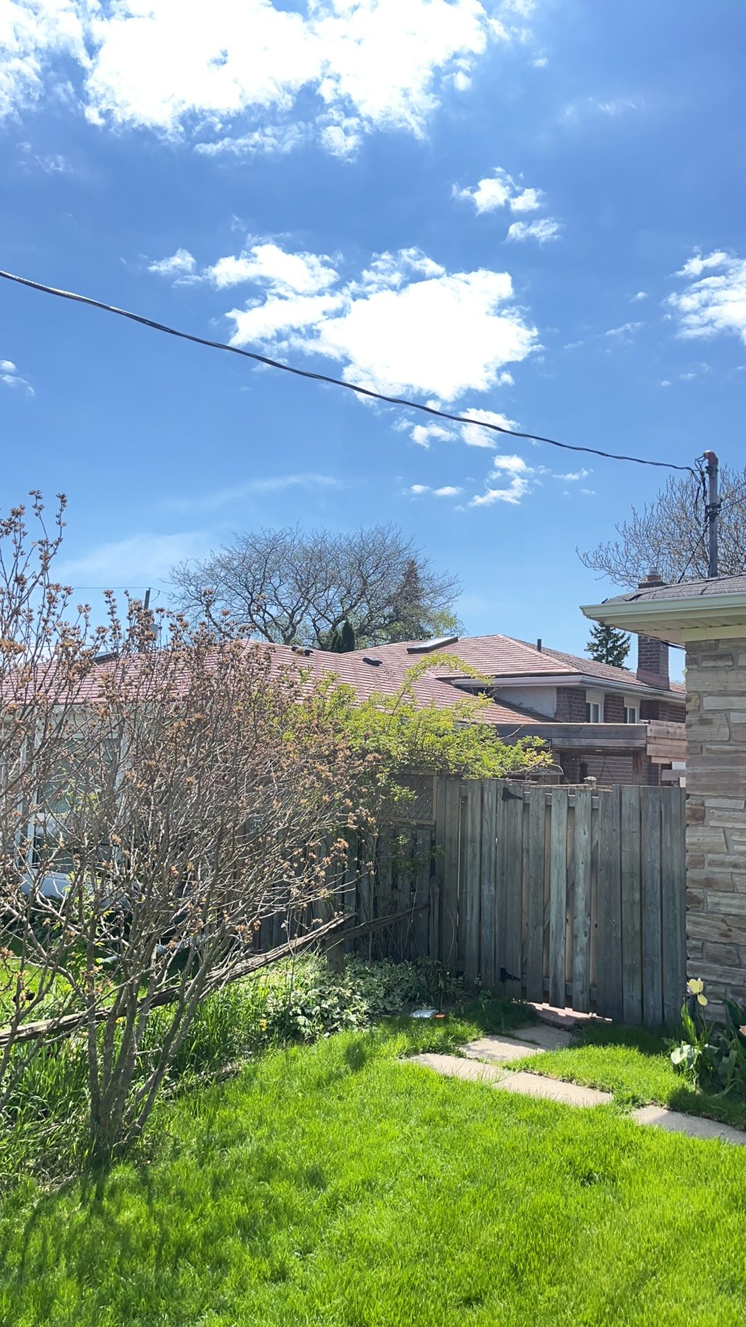 Rear yard view of a suburban single-family home with a hip roof in aged copper Interlock aluminum shingles, partially obscured by fence and shrubs.