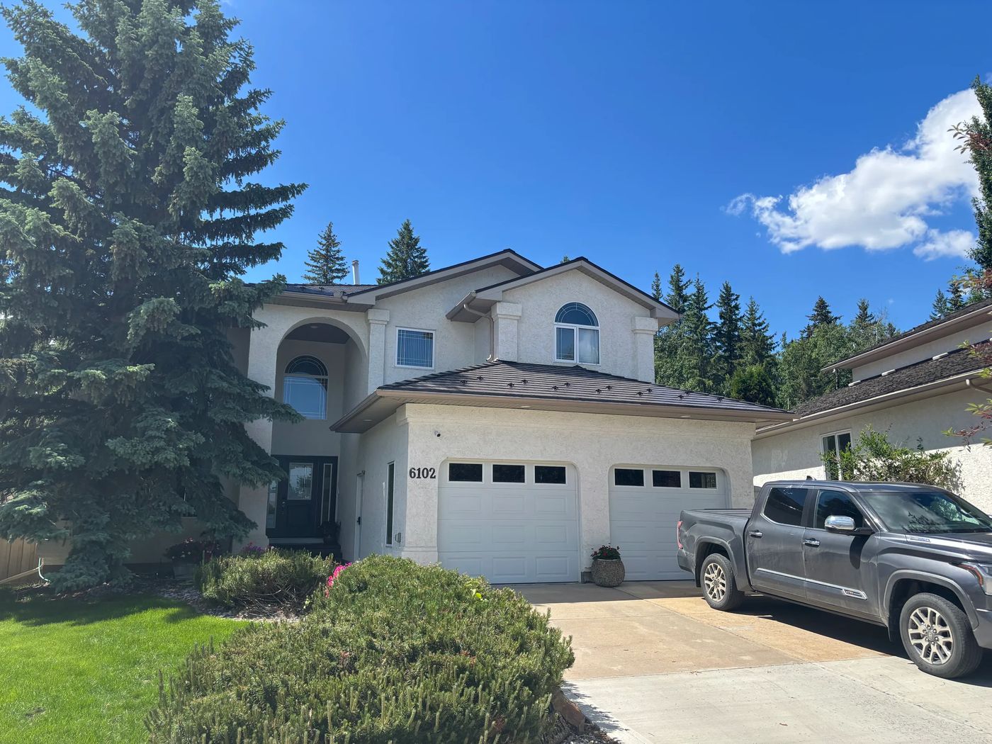 Tudor Brown Interlock Cedar Shingle aluminum roof on a Tudor style house with brown roof among tall trees, Grande Prairie, Alberta