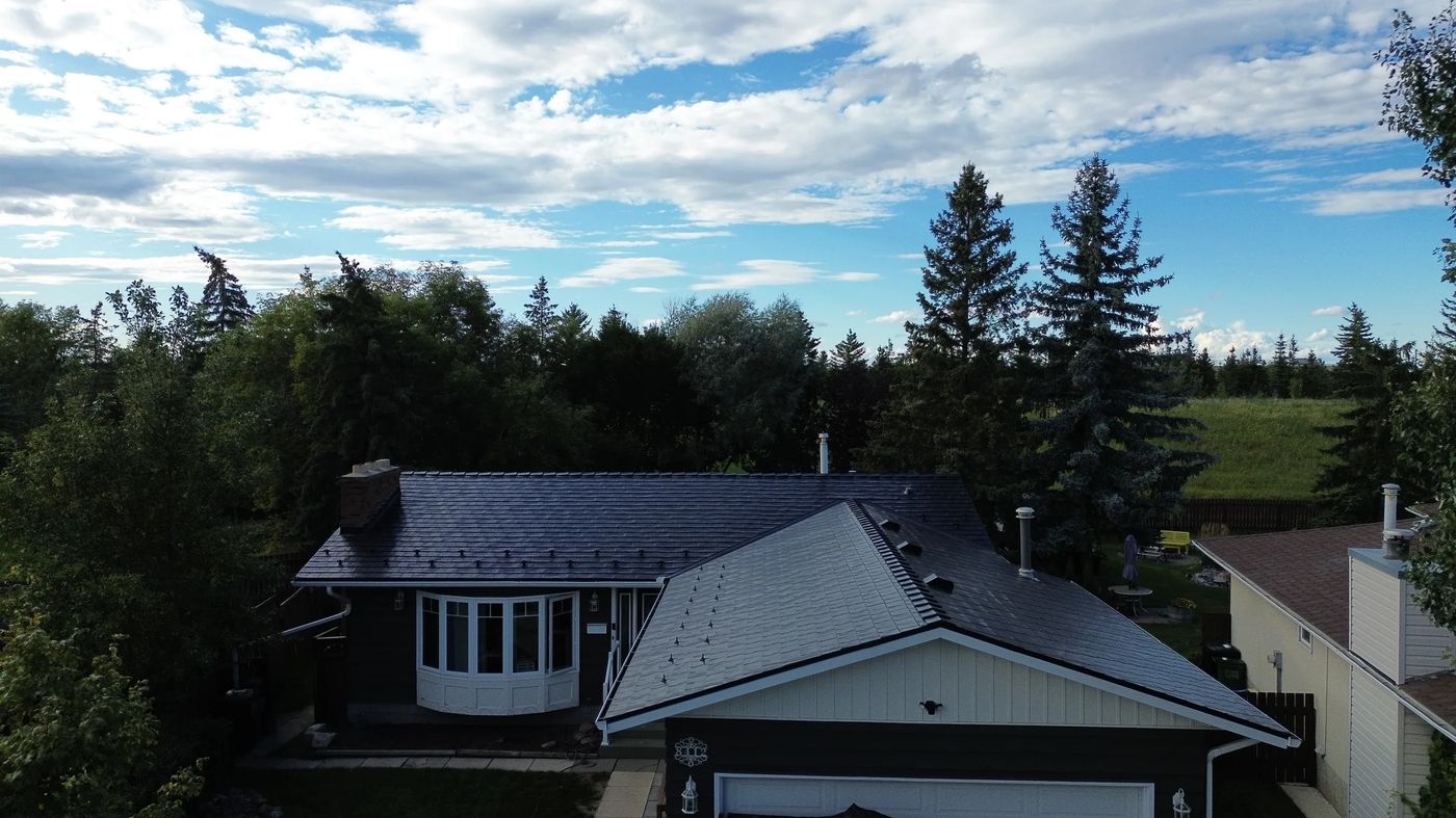 Black Interlock Slate aluminum roof on a black metal roof on a white bungalow among tall trees, Edmonton, Alberta