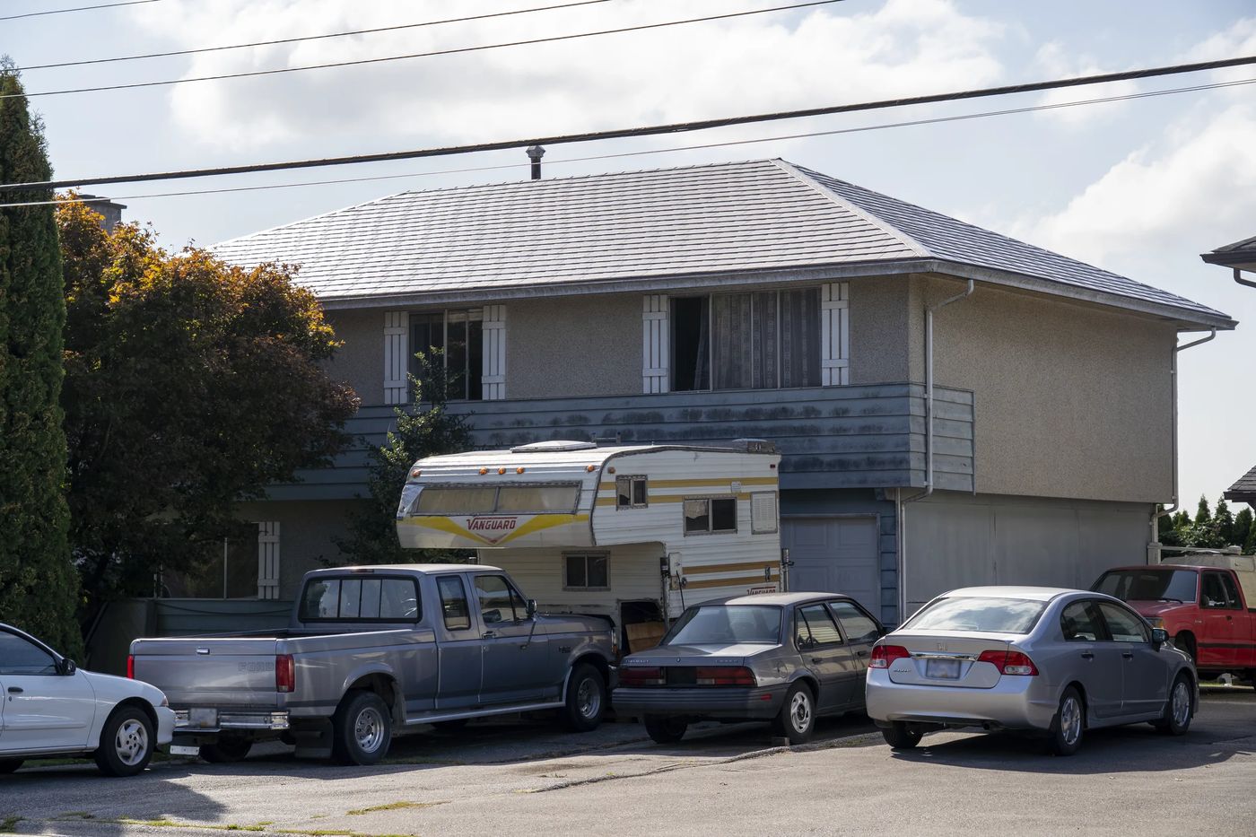 Taupe Interlock Slate aluminum roof on a two-storey taupe home with a metal roof among tall pines, Delta, British Columbia