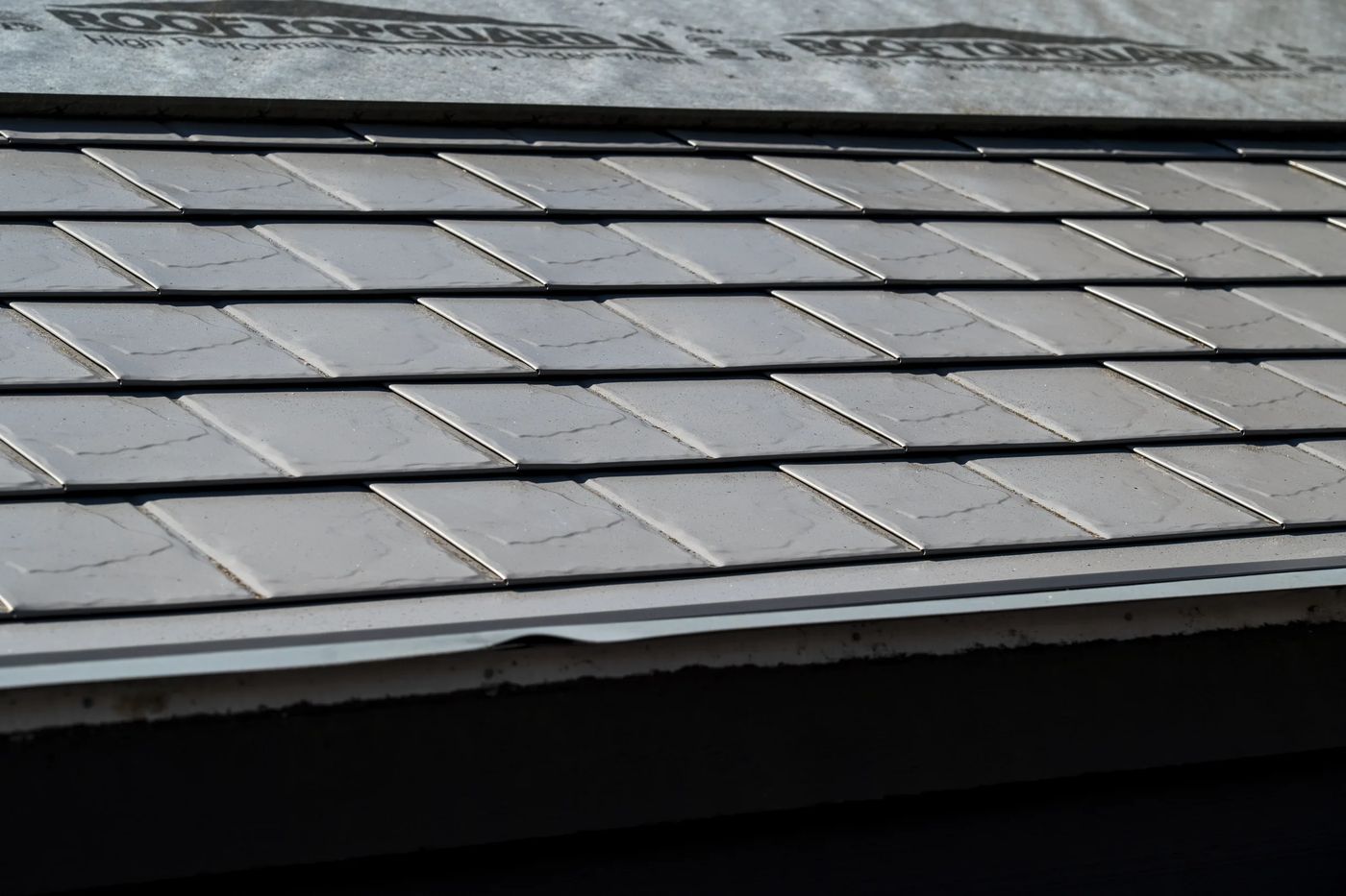 Taupe Interlock Slate aluminum roof on a taupe metal roof on a two-storey home among tall pines, Surrey, British Columbia