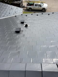 Deep Charcoal Interlock Slate aluminum roof on a modern home with a metal roof among rural fields, Coleman, Alberta