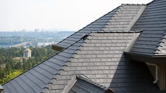 Close-up of a multi-hip deep charcoal Interlock aluminum slate metal roof with complex valleys and ridge caps, overlooking the North Vancouver skyline.