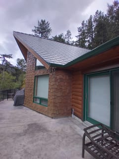 Deep Charcoal Interlock Slate aluminum roof on a brown single-storey chalet with green trim among tall, Juan de Fuca, British Columbia