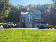 Tile Red Interlock Slate aluminum roof on a grey two-storey home with dormers among tall trees, Granby, Connecticut