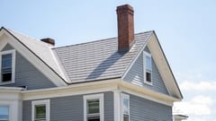 Two-story Victorian home in Musket Grey Interlock aluminum slate roof with twin brick chimneys, dormer windows, and grey vinyl siding.
