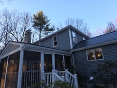 Rear-left view of a two-story colonial home in Westford, MA with Interlock deep charcoal aluminum slate roofing, dormer, and chimney at dusk.