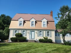 Aged Copper Interlock Shingle aluminum roof on a yellow two-storey Colonial home with dormers among tall, Wrentham, Massachusetts