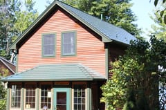 Hunter Green Interlock Slate aluminum roof on a red two-storey cottage with dormers among tall green trees, Pelham, New Hampshire