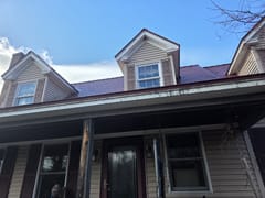 Colonial home in Deerfield NH with Interlock aluminum slate roof in Tile Red, featuring three dormers, covered front porch, and brick chimney.