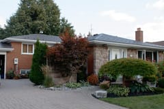 Ranch-style brick and stone home in Scarborough with Interlock Tudor Brown aluminum slate roof, hip profile, brick chimney, and lush landscaped front yard.