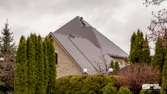 Large two-storey stone home with a steeply pitched multi-hip Interlock aluminum slate roof in Tudor Brown, featuring skylights and complex valleys.