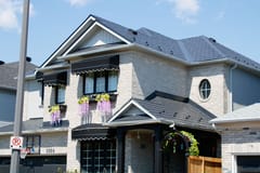 Two-storey suburban home in Milton, ON with a complex multi-hip black Interlock aluminum slate metal roof, snow guards, black awnings, and wisteria window boxes.