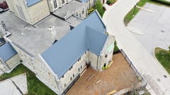 Aerial view of a deep charcoal Interlock aluminum slate metal roof on a historic stone church in Toronto, featuring complex multi-gable geometry and a stone chimney.