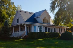 1.5-storey Craftsman home in Cannifton, ON with deep charcoal Interlock aluminum slate metal roof featuring dormers, wraparound porch, and arched upper window.