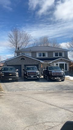 Two-storey brick Colonial home in Bradford, ON with black Interlock aluminum slate metal roofing, double garage, and three black trucks in the driveway.