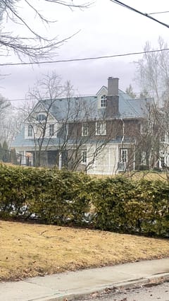 Two-storey colonial brick home in Burlington ON with steep deep charcoal Interlock aluminum slate roof, twin dormers, and brick chimney, viewed from street.