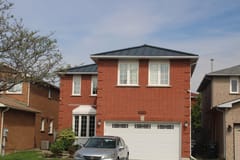 Two-storey red brick home in Mississauga with a low-pitch hip roof finished in black Interlock aluminum standing seam metal roofing.