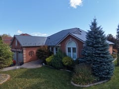 Musket Grey Interlock Cedar Shingle aluminum roof on a red ranch style home with a grey metal roof among tall, Brampton, Ontario