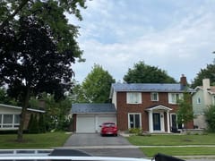 Two-storey Colonial brick home in Ottawa with Interlock black aluminum slate metal roofing on main house and attached garage, set in a leafy suburban neighbourhood.