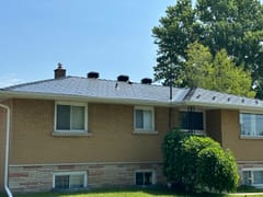 Black Interlock aluminum slate metal roof on a single-storey ranch-style brick home in Cornwall, ON, featuring multiple roof louvers and a brick chimney.