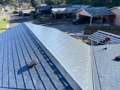 Aerial view of a deep charcoal Interlock aluminum slate metal roof with hip planes, valley, and vent on a single-story ranch home in Florence, OR.