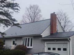 Cape Cod home in South Burlington VT with Interlock deep charcoal aluminum slate metal roof, prominent brick chimney, and gray vinyl siding.