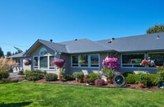 Single-story ranch home in Sequim, WA with Interlock deep charcoal aluminum slate metal roofing, multi-hip profile, and lush hanging flower baskets.