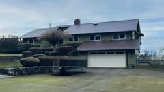 Two-story green ranch-style home in Vancouver WA with Interlock Colonial Brown cedar shingle metal roofing, chimney, and manicured topiary shrubs.