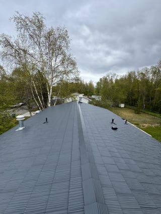 A modern single-family home with a dark gray metal roof and a few vents and a chimney.