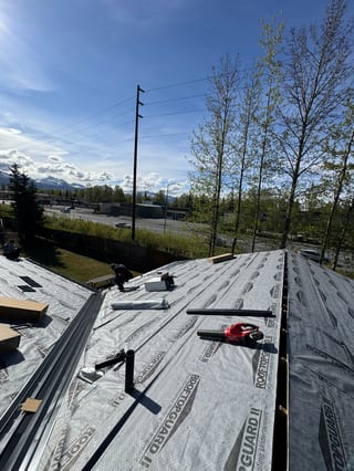 Metal roof installation in progress, with underlayment laid down and partially covered.