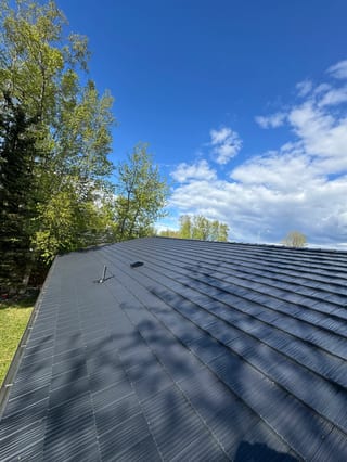 A metal roof installed by Interlock on a ranch-style single-family home in a suburban or urban area on a sunny day.