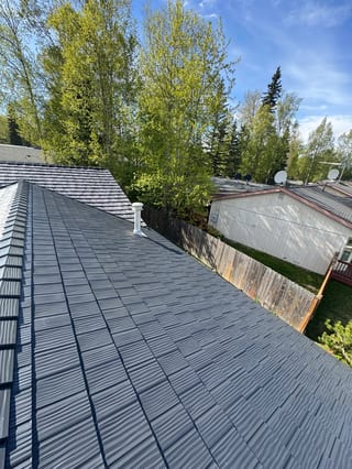 Metal roof on a ranch-style home with a lush green yard and blue sky