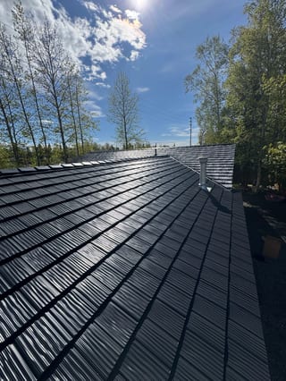 A modern metal roof on a single-family home in an urban or suburban setting, possibly with a blue sky or overcast conditions.
