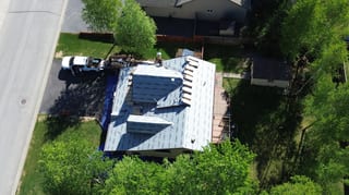 Aerial view of a modern, single-family home with a metal roof and lush greenery.
