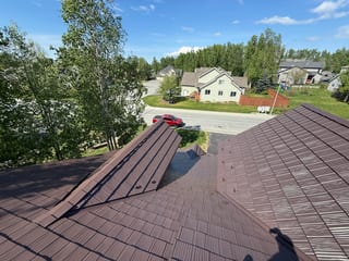 A modern single-family home with a brown metal roof in a suburban neighborhood with trees.