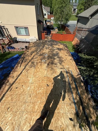 A new metal roof is being installed on a modern single-family home in a suburban area with lush greenery.