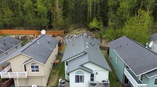 Aerial view of a modern-style single-family home with a metal roof in a wooded area.