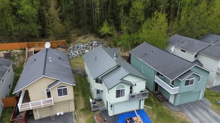 Aerial view of a two-story home with a metal roof, in a forested area with lush greenery