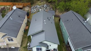 Aerial view of a house with a grey metal roof in a forested rural setting
