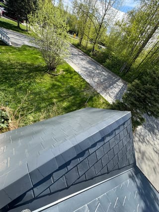 Modern metal roof with grey panels on a single-family home in an urban setting.