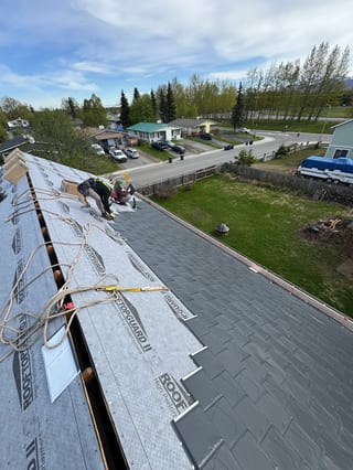 Metal roof under construction with grey shingles and a modern single-family home in the background