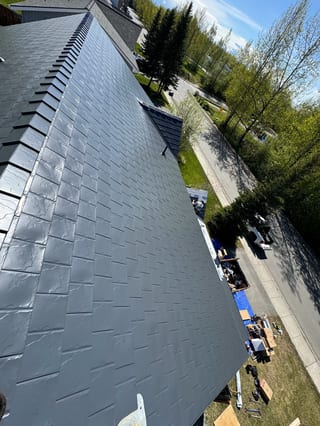 A grey metal roof on a grey house with a grey street in the background.