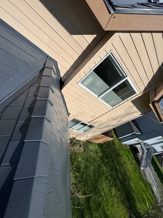 A modern-style single-family home with a metal roof and snow guards, situated in an urban or suburban area with lush greenery.